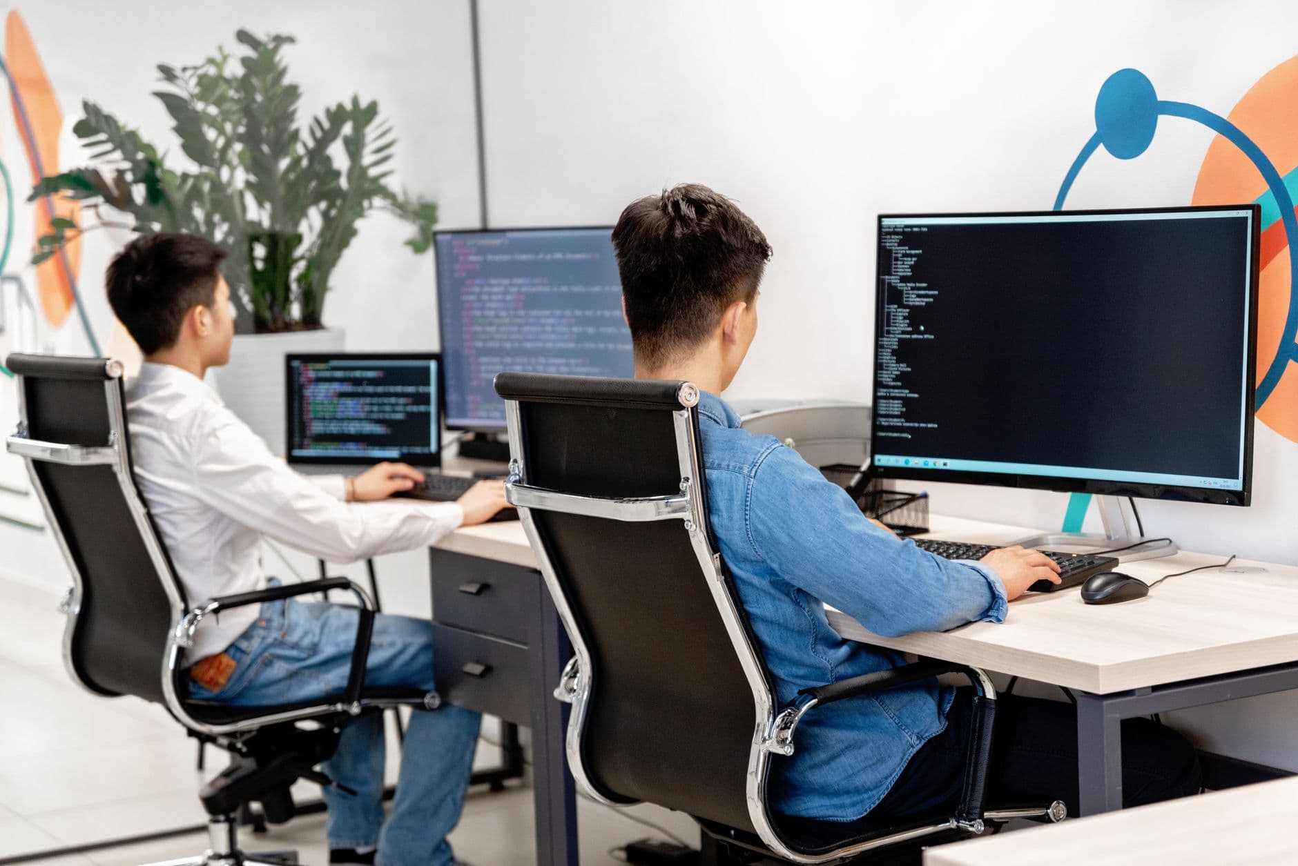 Two developers programming at desks with multiple screens in a modern office
